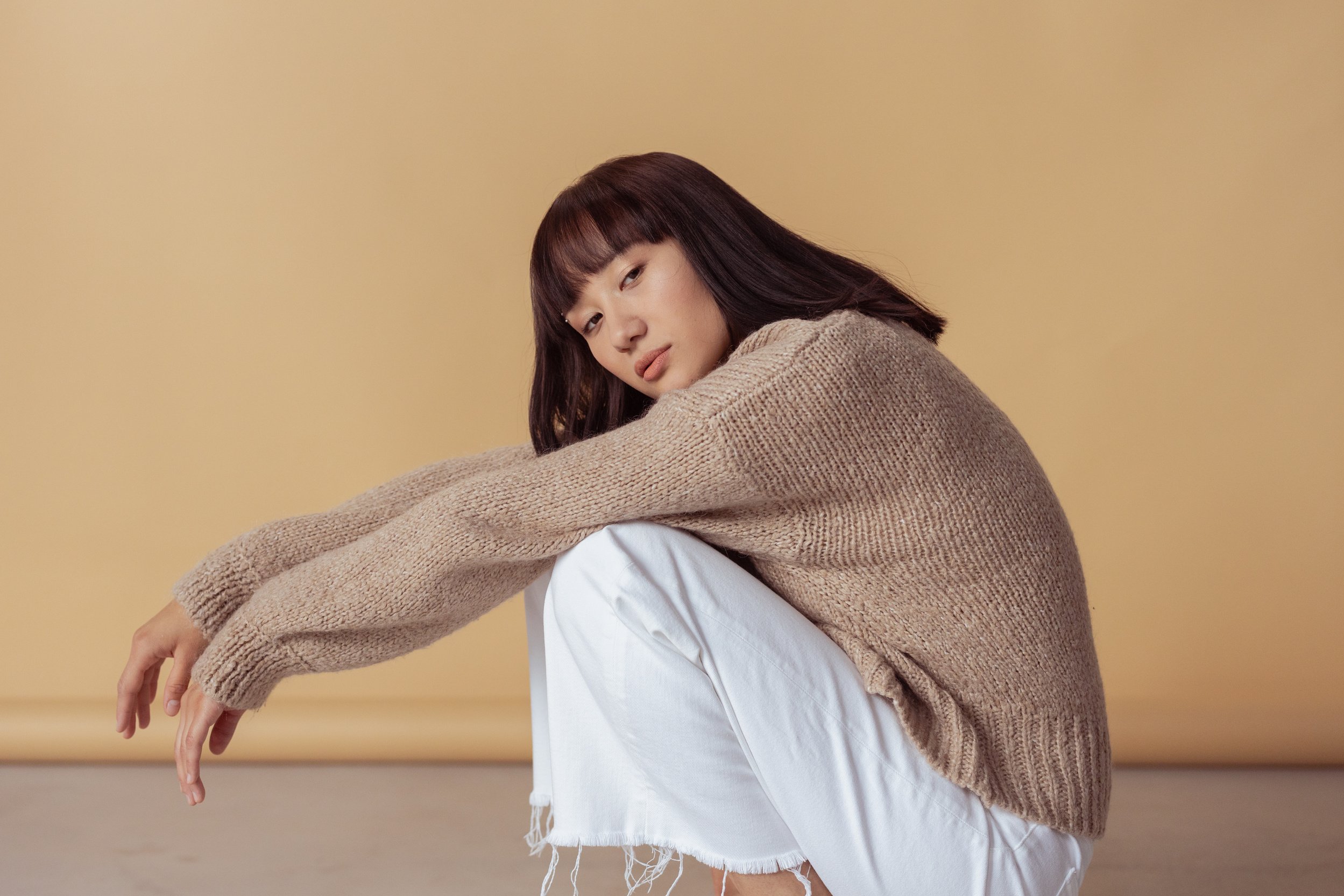 A Woman in Brown Sweater and White Pants Squatting on the Floor